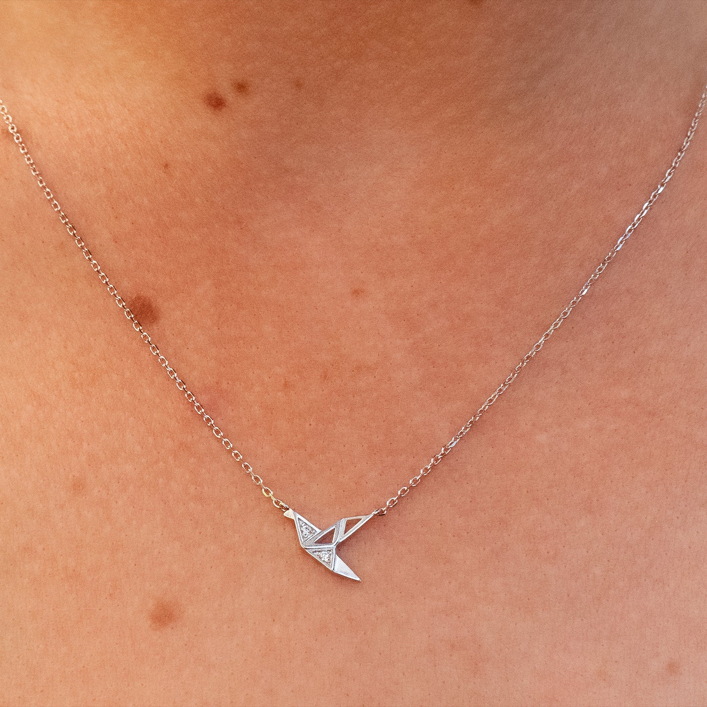 Close-up de cuello de mujer usando collar de grulla tipo origami con circones