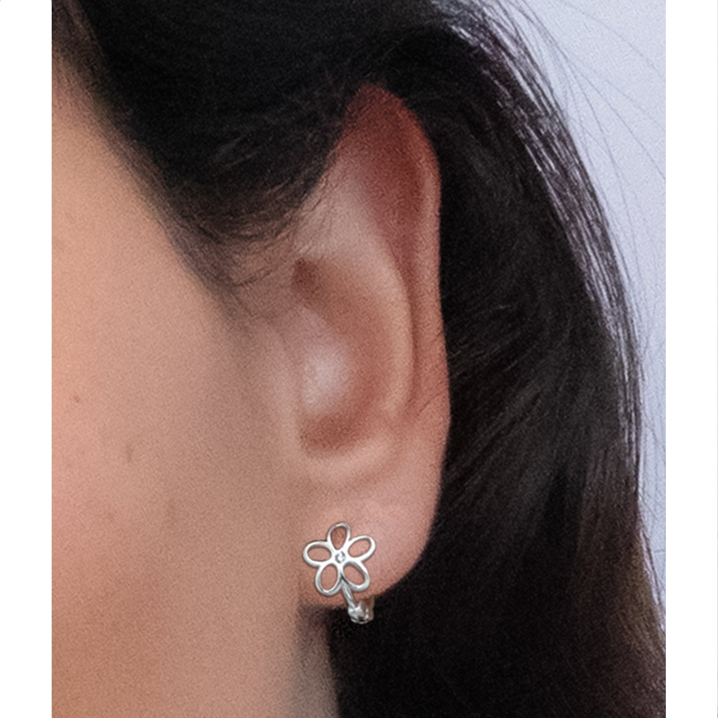 Primer plano de oreja con argolla plateada con flor y circón