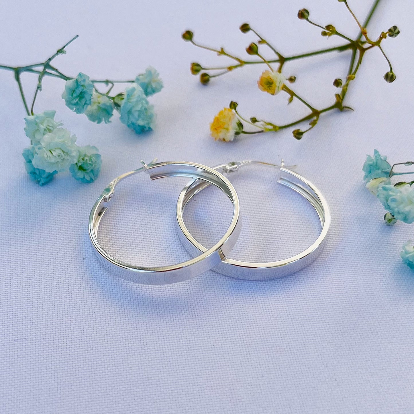 Par de argollas planas de plata de 30 mm en fondo blanco con flores secas