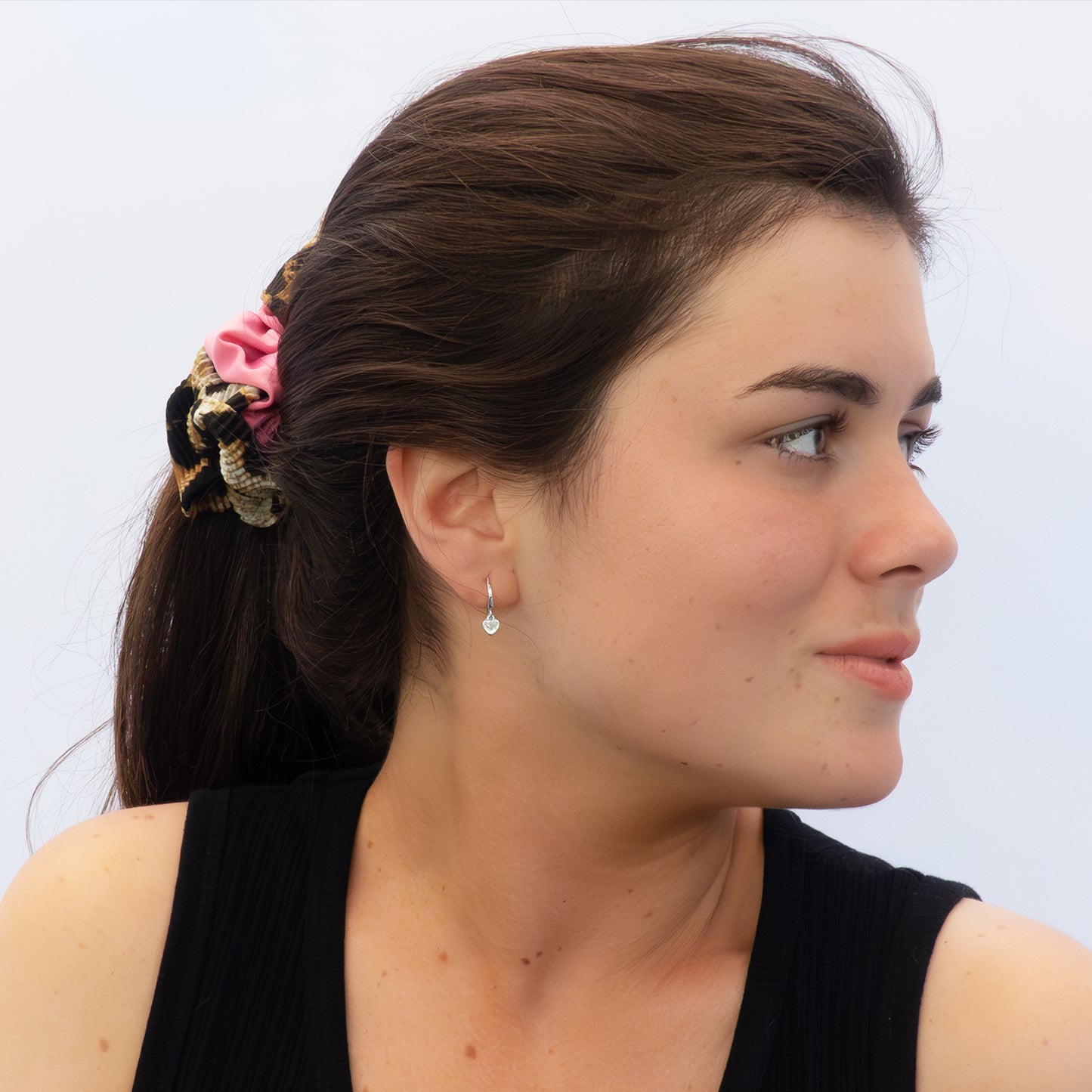 Mujer de perfil usando pendientes plateados con colgante de corazón.