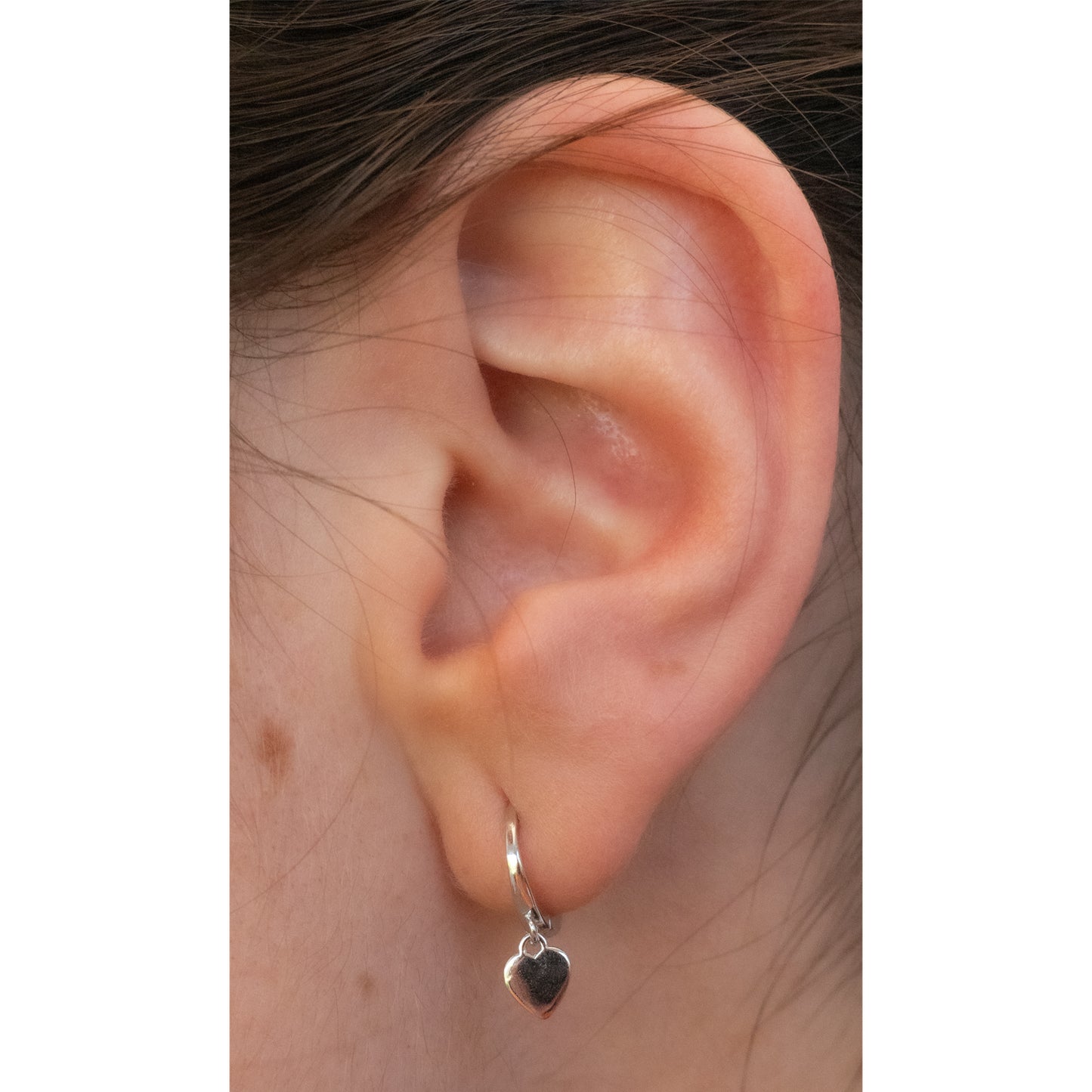 Oreja con pendiente plateado con corazón.