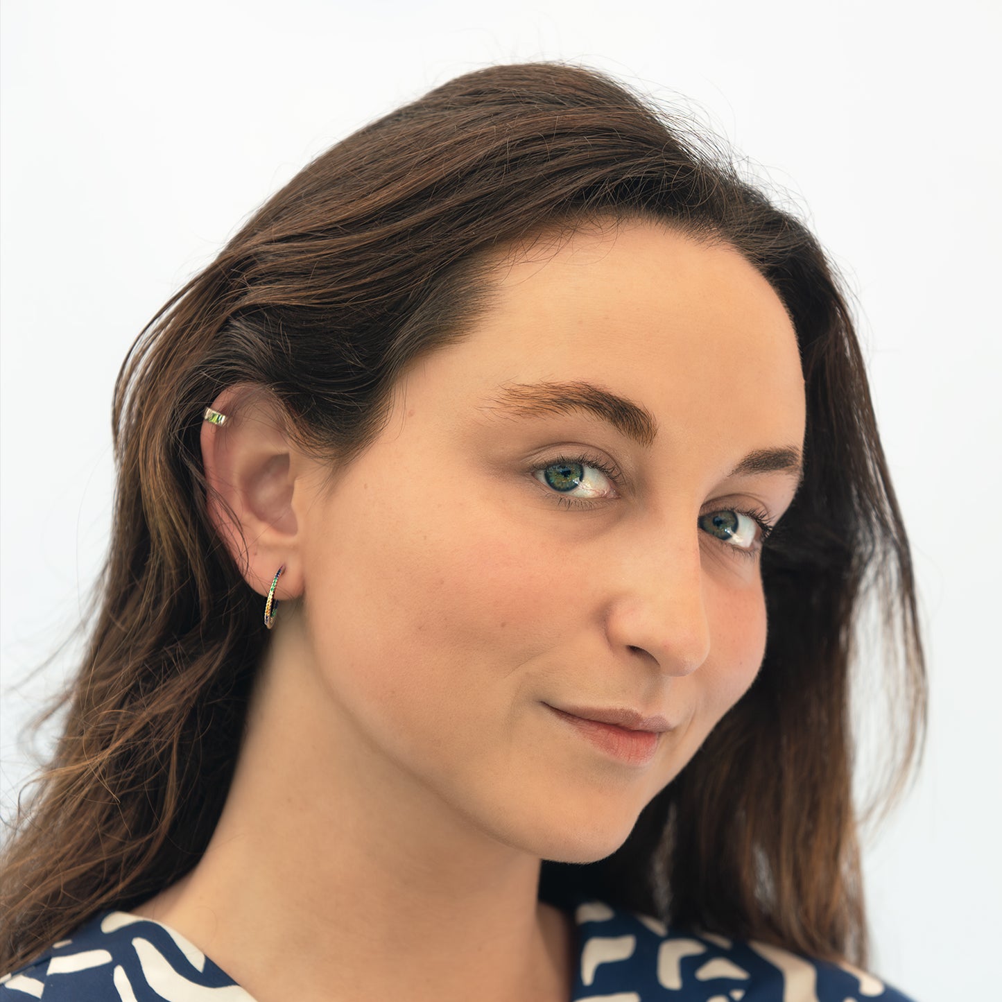 Mujer de cabello castaño usando earcuff de plata y arete colgante.