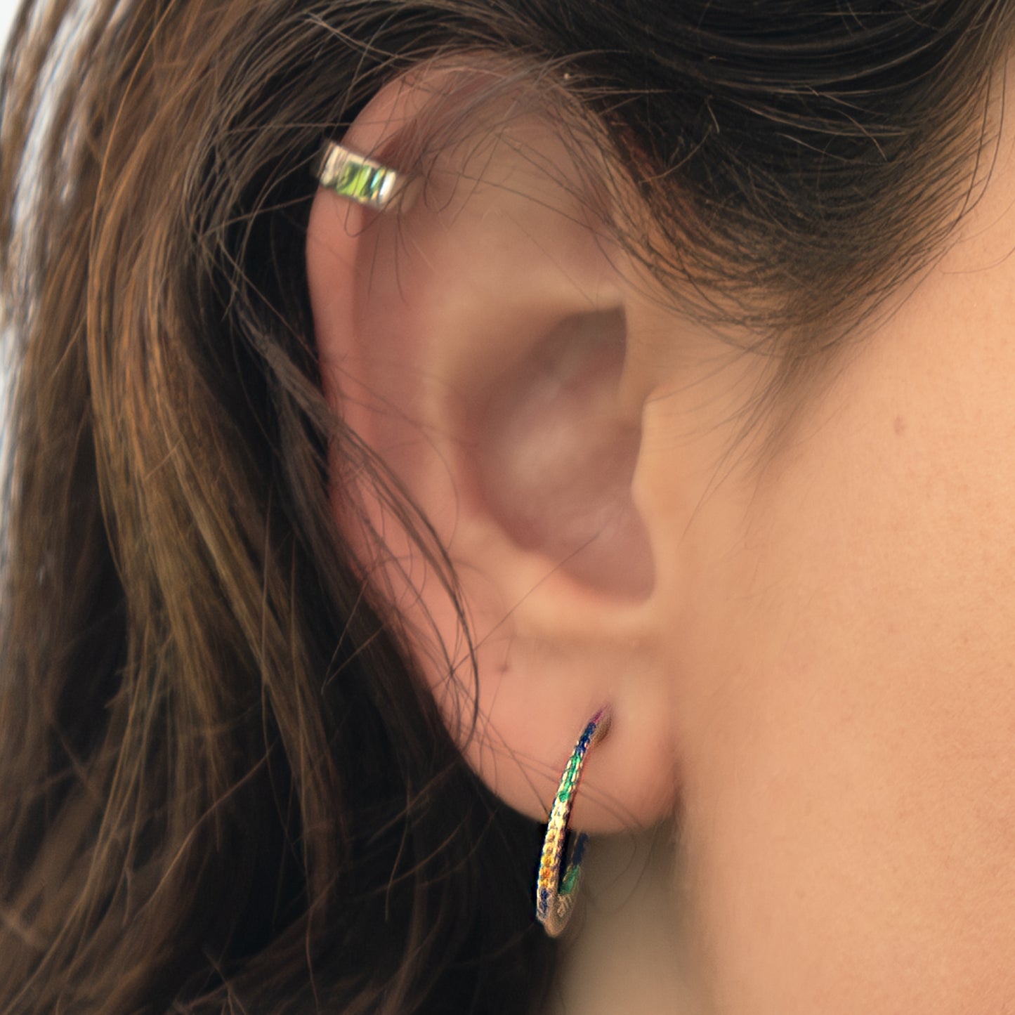 Primer plano de oreja con earcuff de plata y arete colgante.