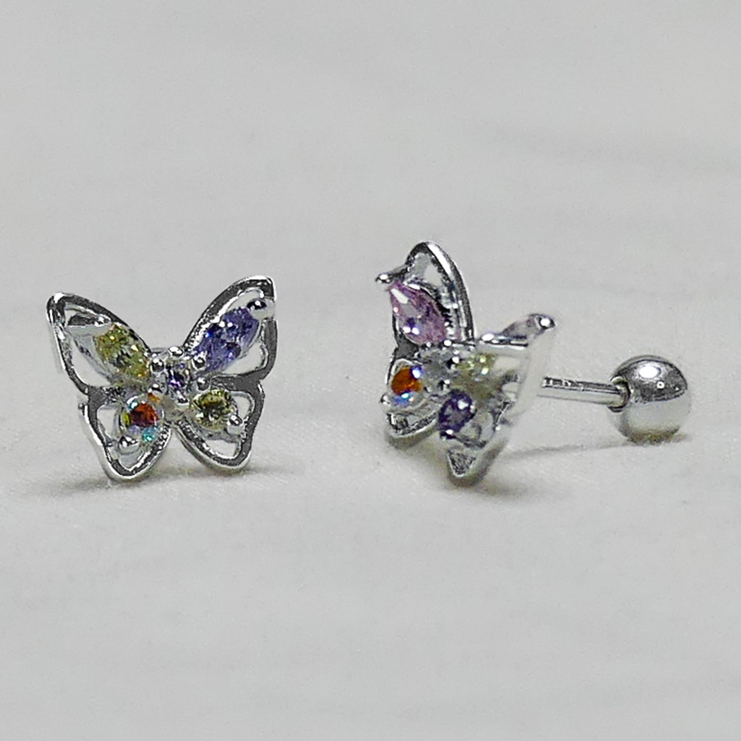 Par de pendientes en forma de mariposa con circones de colores vistos en diagonal sobre fondo gris.
