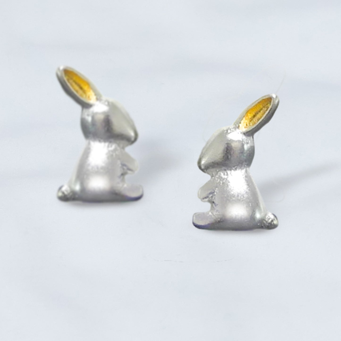 Par de Aritos de plata y oro, en en forma de conejito de perfil plateado con orejas doradas sobre fondo gris