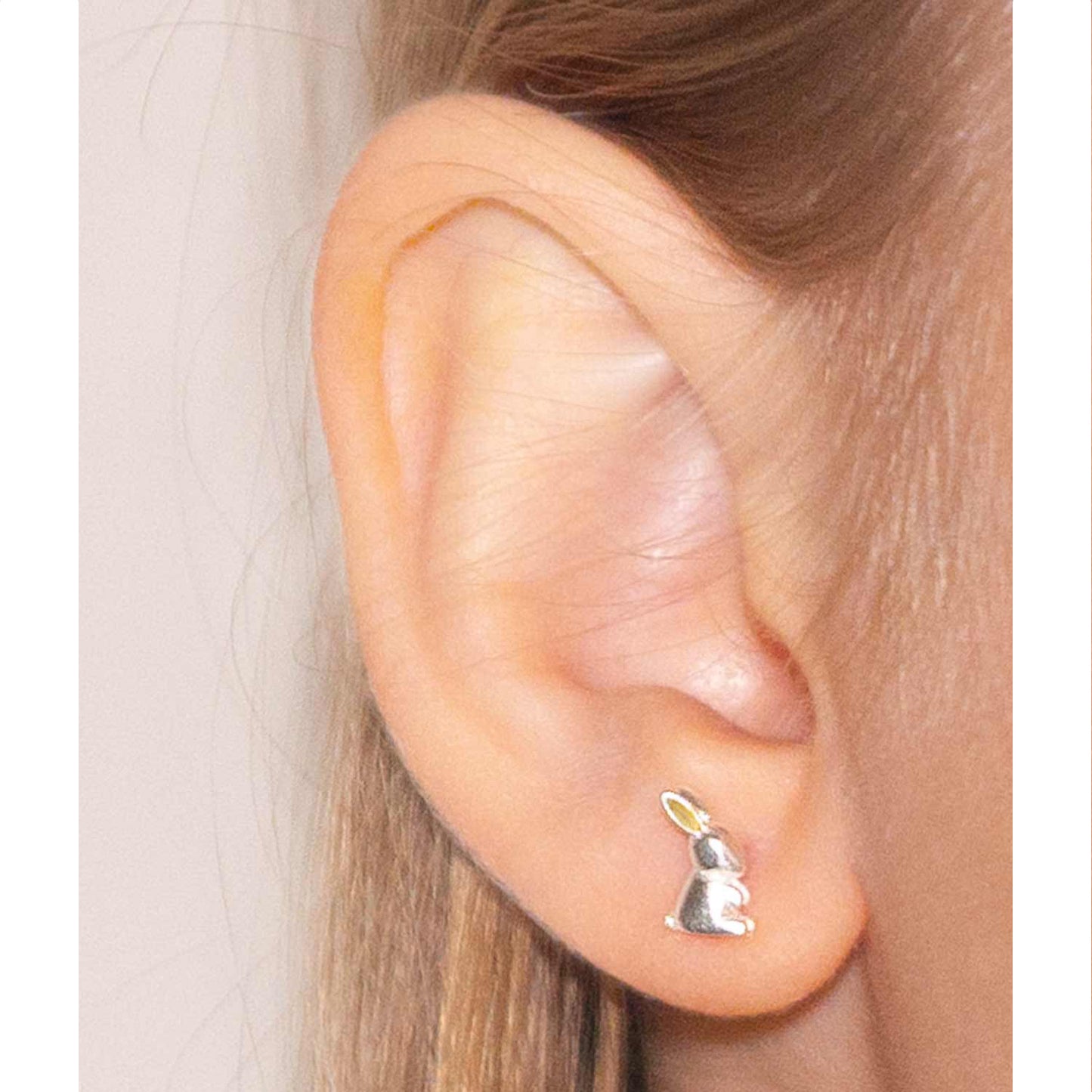 Primer plano de oreja con arito de plata y oro, en en forma de conejito de perfil plateado con orejas doradas
