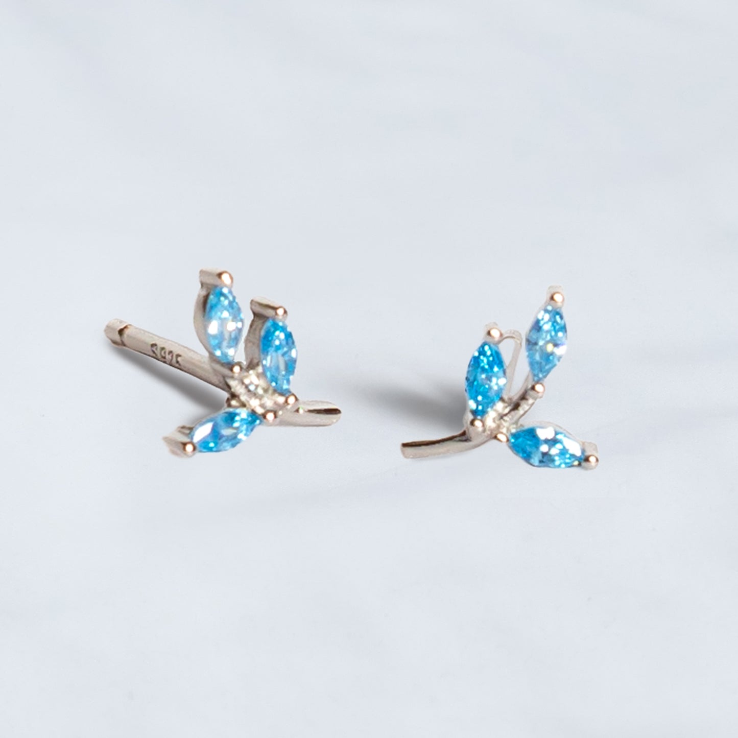 Par de Aros de plata en forma de ramita con hojas formadas por circones azules, sobre fondo gris