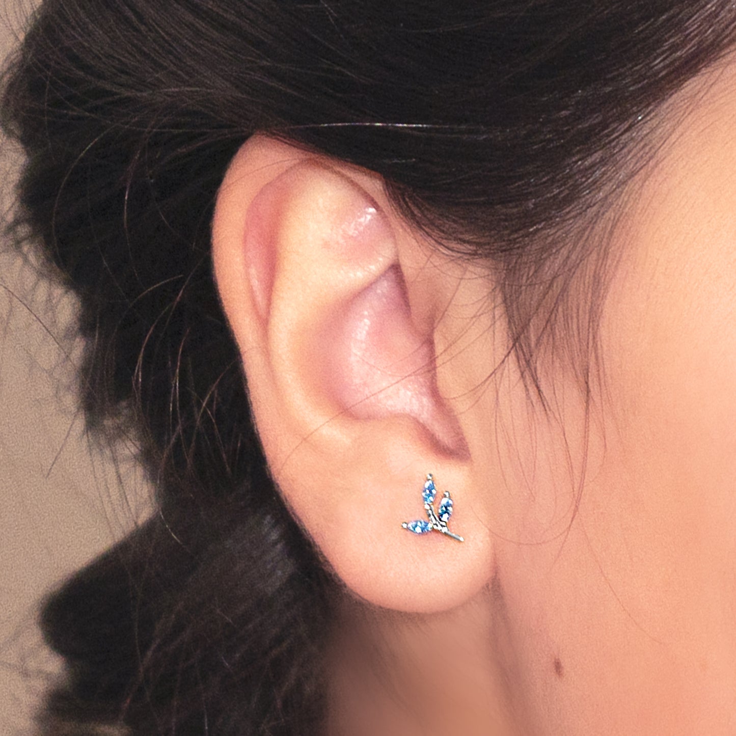 Detalle de oreja con aros de plata en forma de ramita con hojas formadas por circones azules