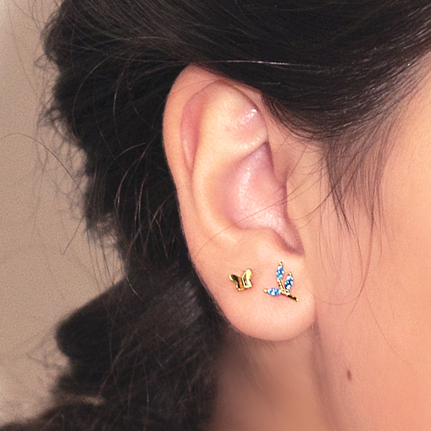 Detalle de oreja con aro de plata bañado en oro, en forma de ramita con hojas formadas por circones azules