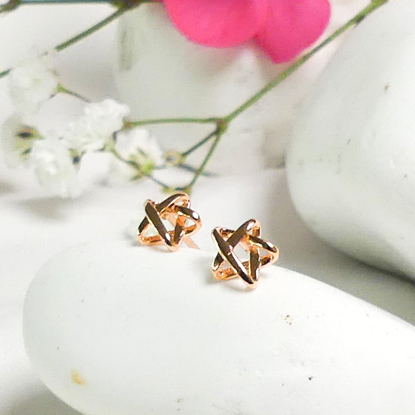 Par de aros con forma de estrella tridimensional rose gold sobre piedras blancas con flores