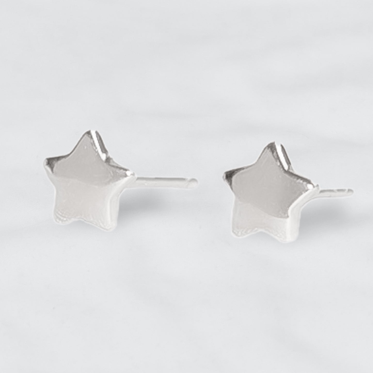 Par de Aros de plata en forma de estrella maciza sobre fondo gris claro