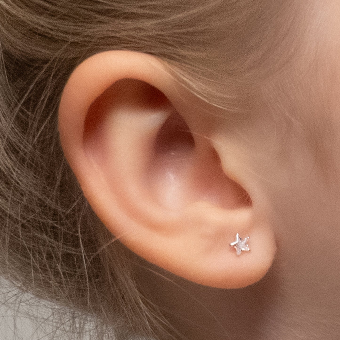 Close-up de oreja de niña con aros de estrella plateada y cristal.