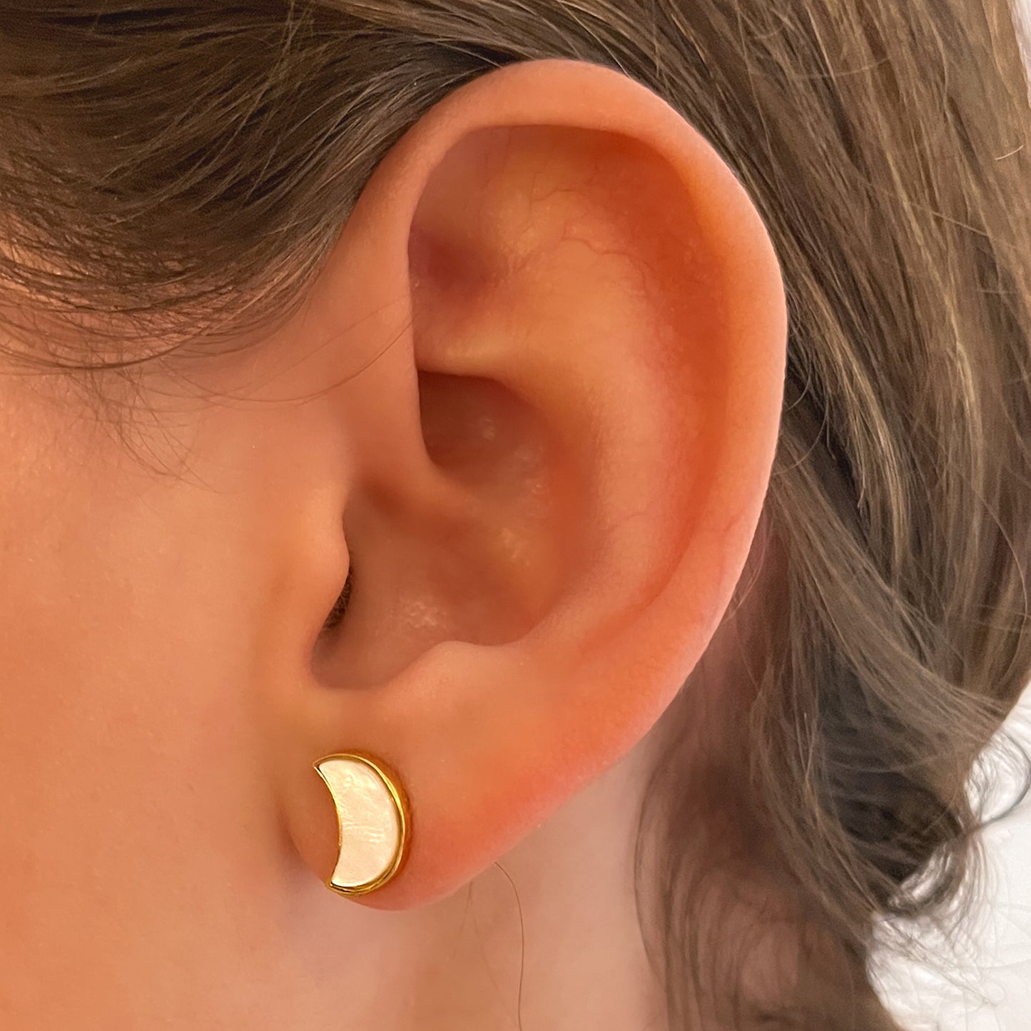 Primer plano de oreja con aro de plata bañado en oro, con luna creciente en nácar