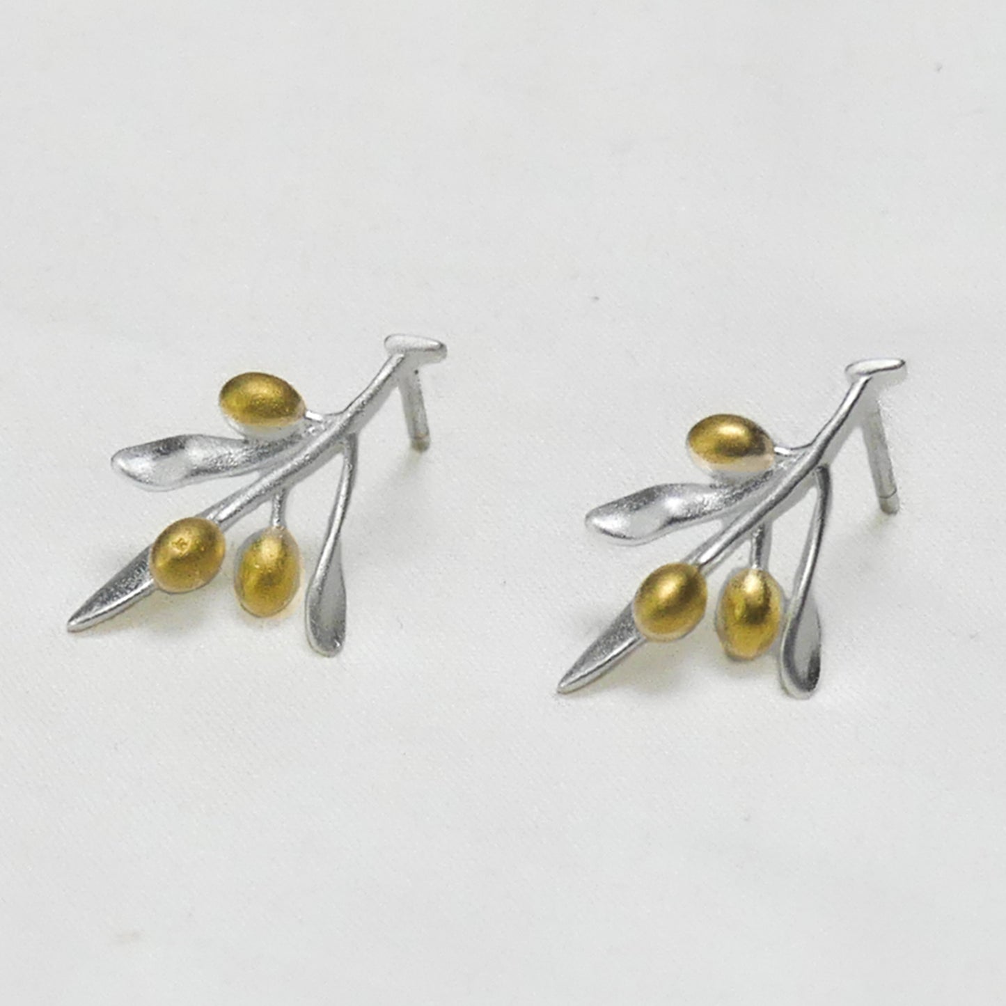 Par de aros de plata en forma de rama de olivo con frutos bañados en oro, sobre fondo gris