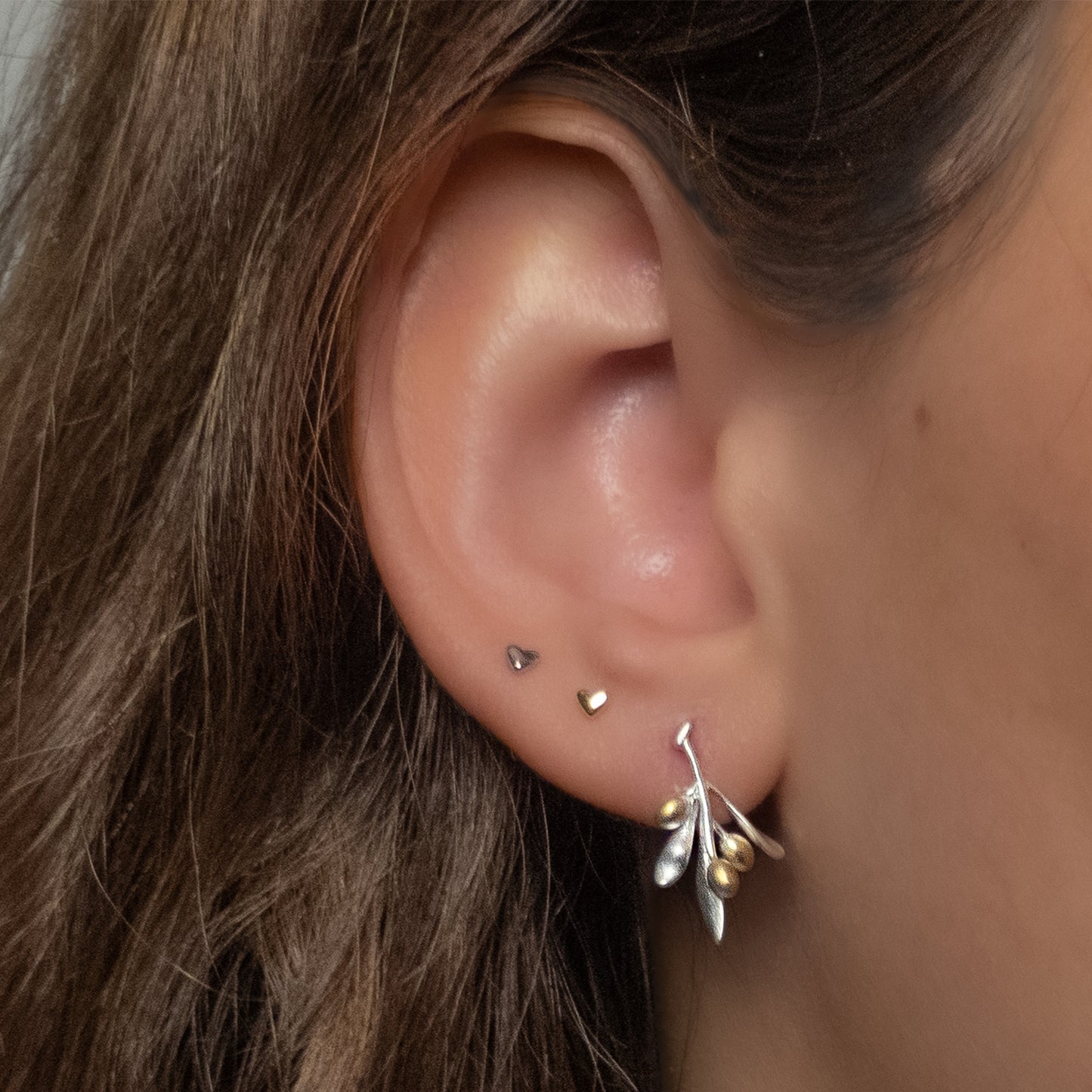 Primer plano de oreja con aro de plata en forma de rama de olivo con frutos bañados en oro