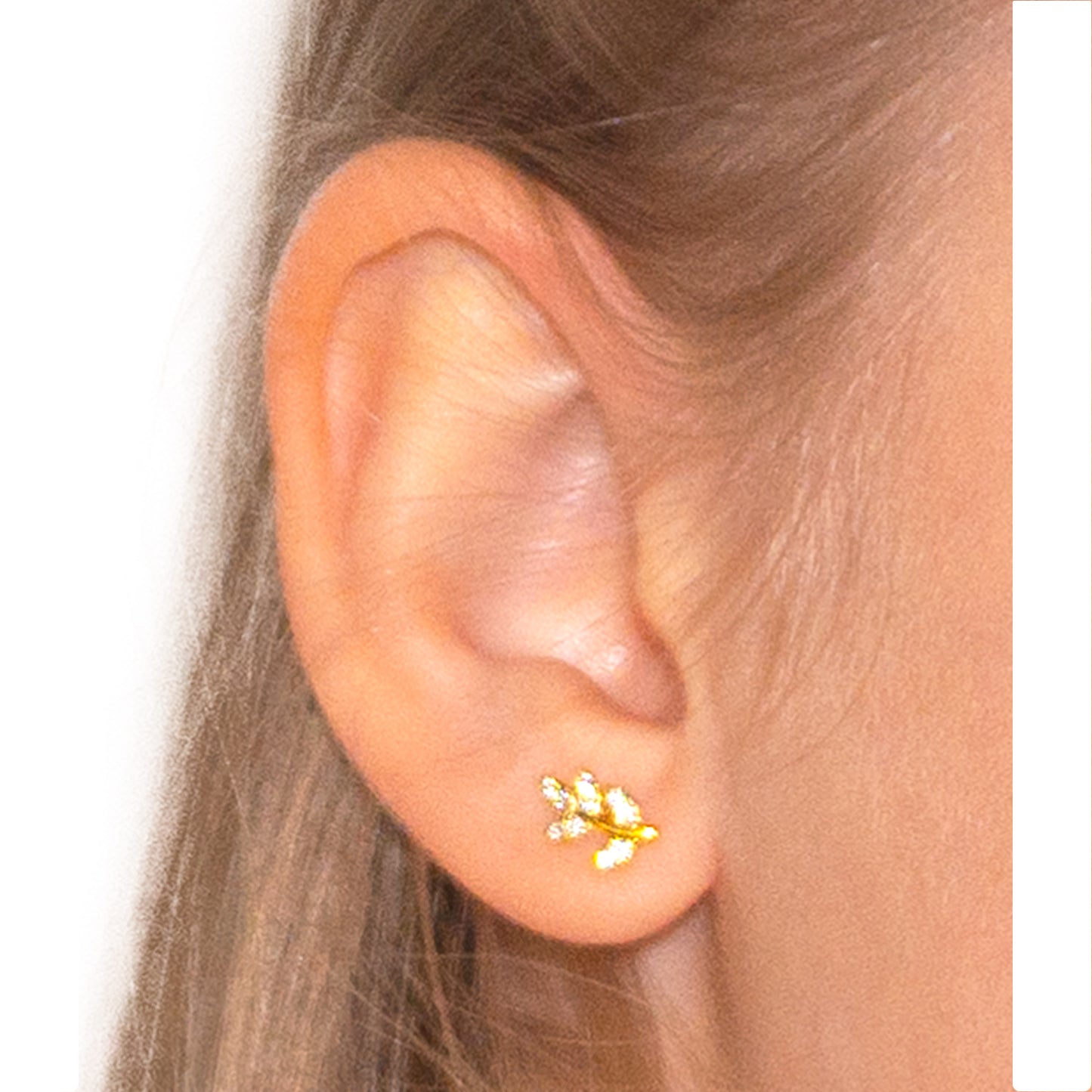 Primer plano oreja con aro de plata bañado en oro en forma de hoja con circones blancos