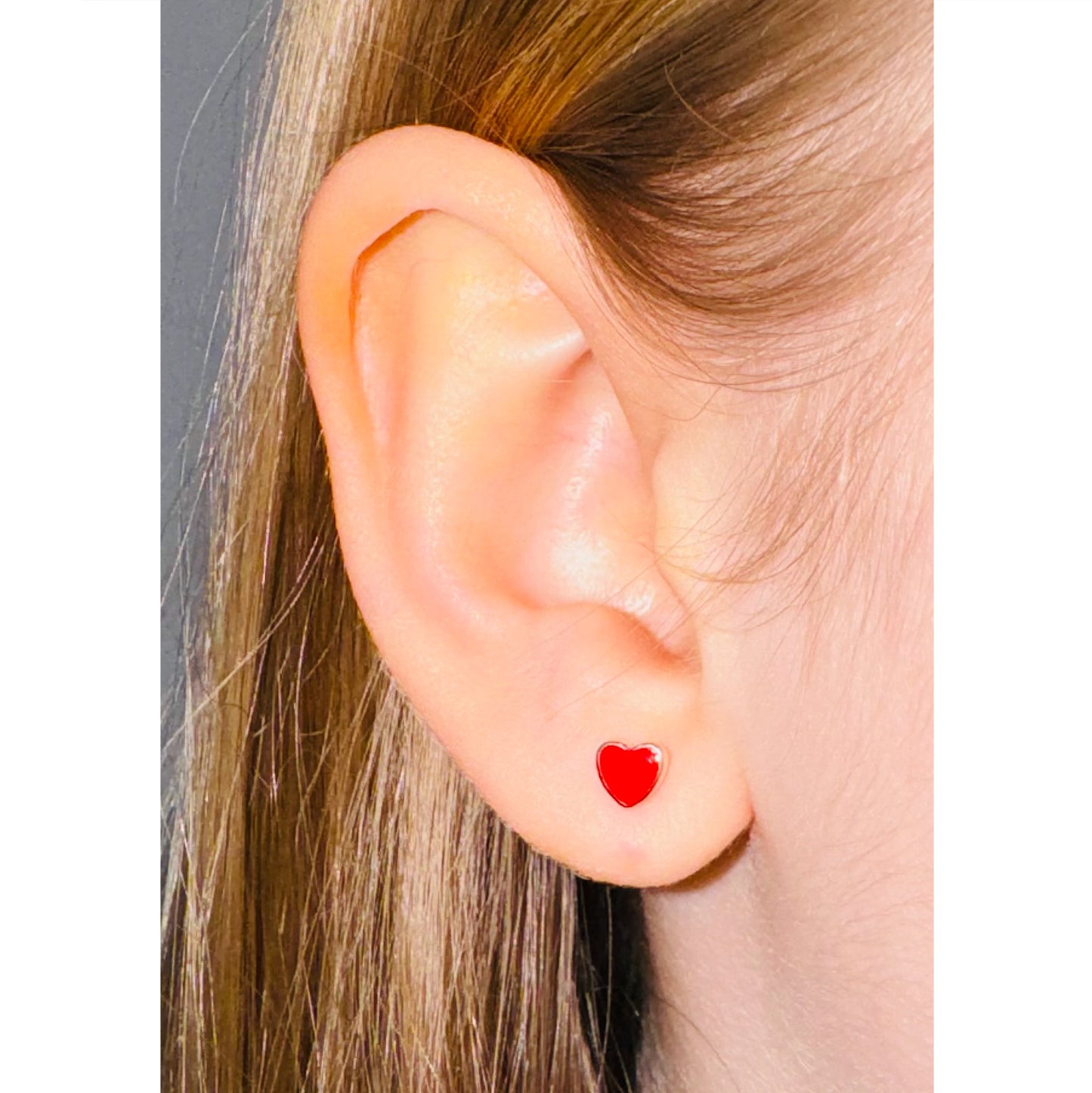 Primer plano de oreja de niña con arito de corazón rojo.