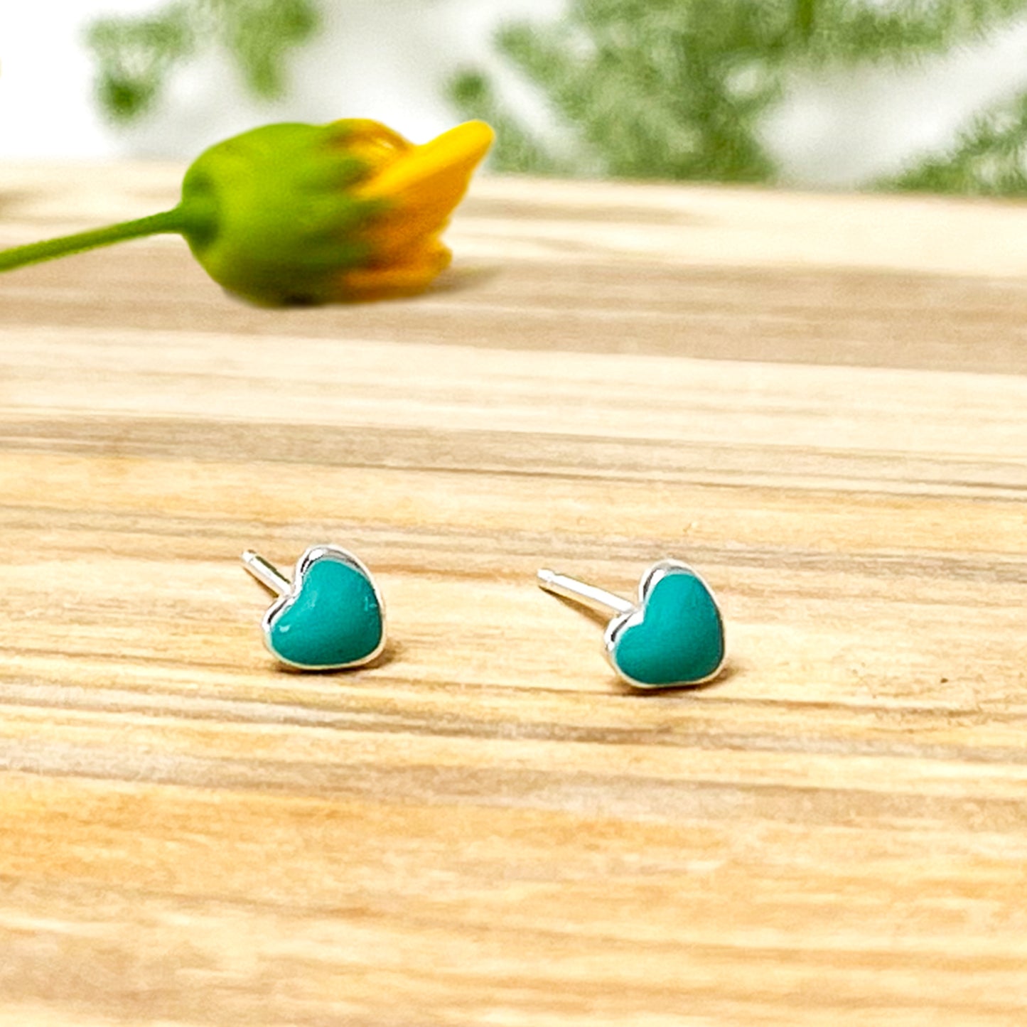 Par de pendientes de corazón turquesa sobre superficie de madera.