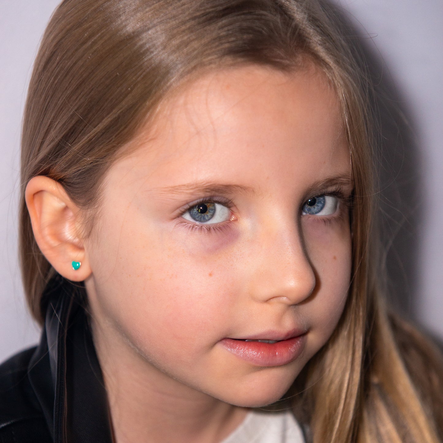 Niña rubia llevando pendientes de corazón turquesa.