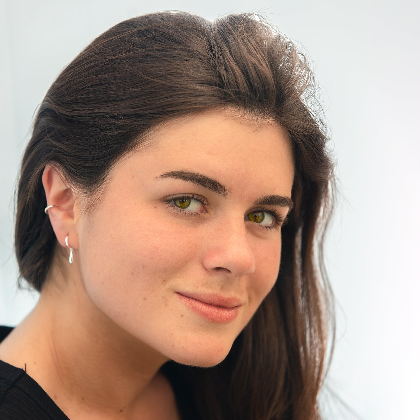 Mujer de cabello oscuro usando earcuff plateado con circones blancos y aro pequeño