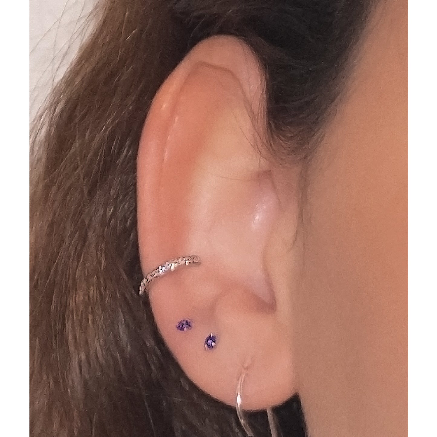Primer plano oreja con earcuff plateado con circones y otros pendientes.