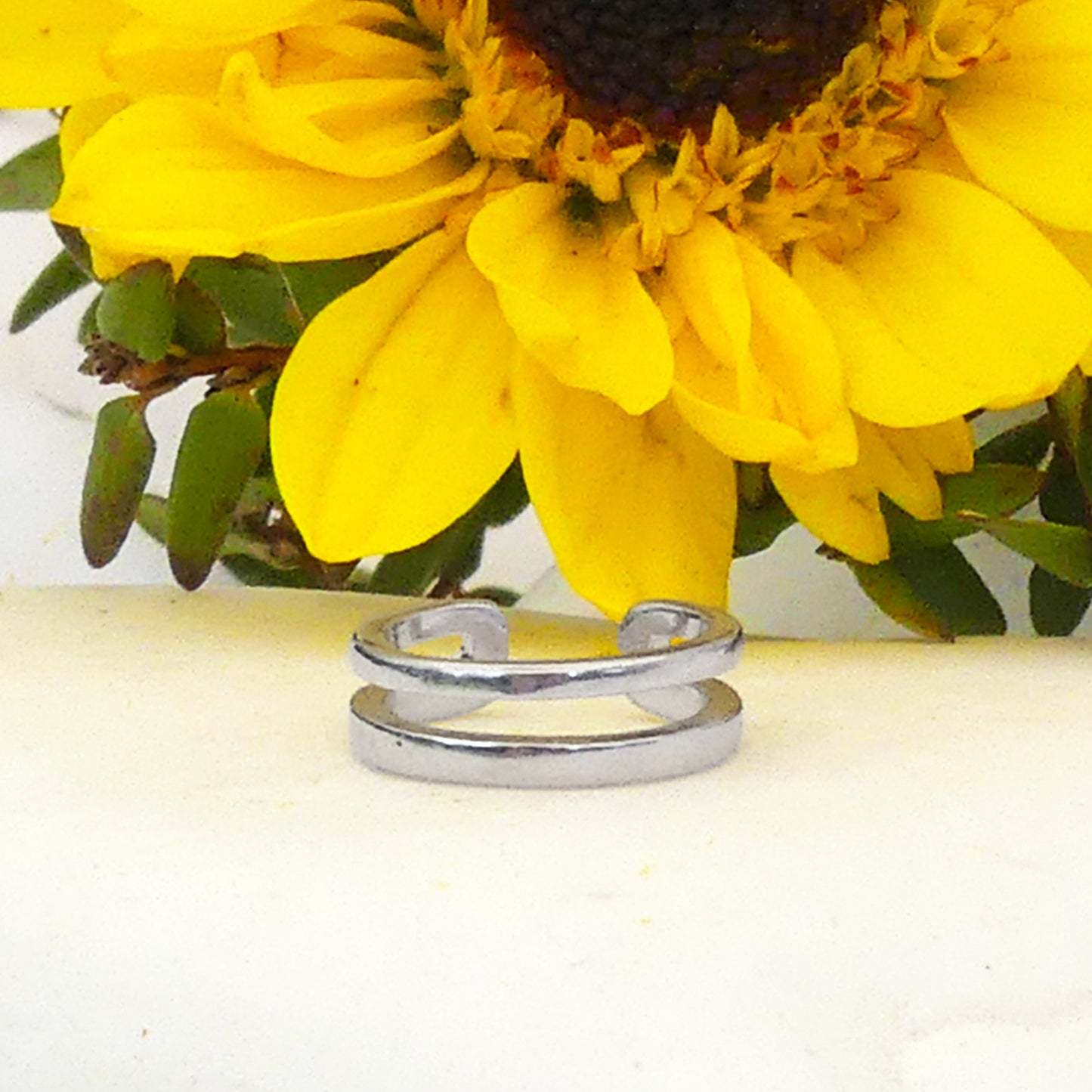 Earcuff doble de plata sobre superficie blanca con girasol