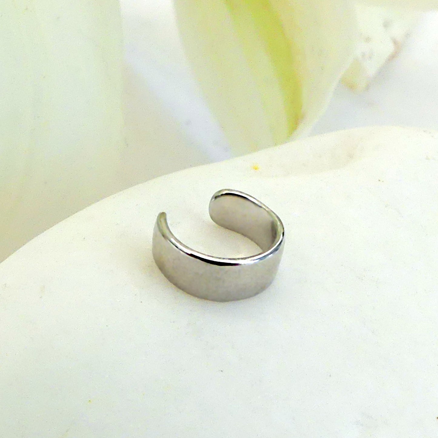 Earcuff de plata sobre piedra blanca con hojas pálidas al fondo.