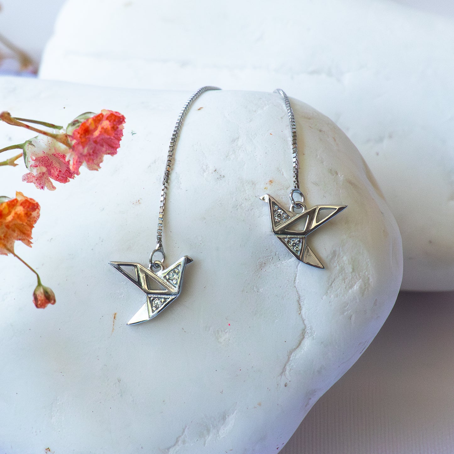 Aros largos plateados con cadena y colgante de grulla tipo origami con circones blancos.