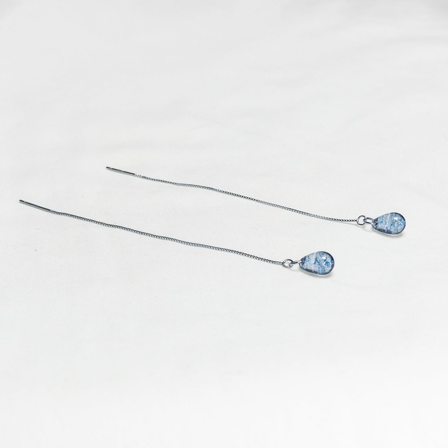 Par de aros con gotas azules y cadenas delgadas sobre fondo blanco