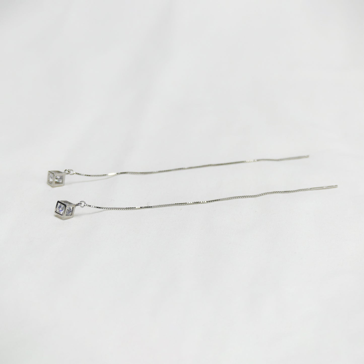 Par de pendientes de cubo con cadena larga sobre fondo blanco