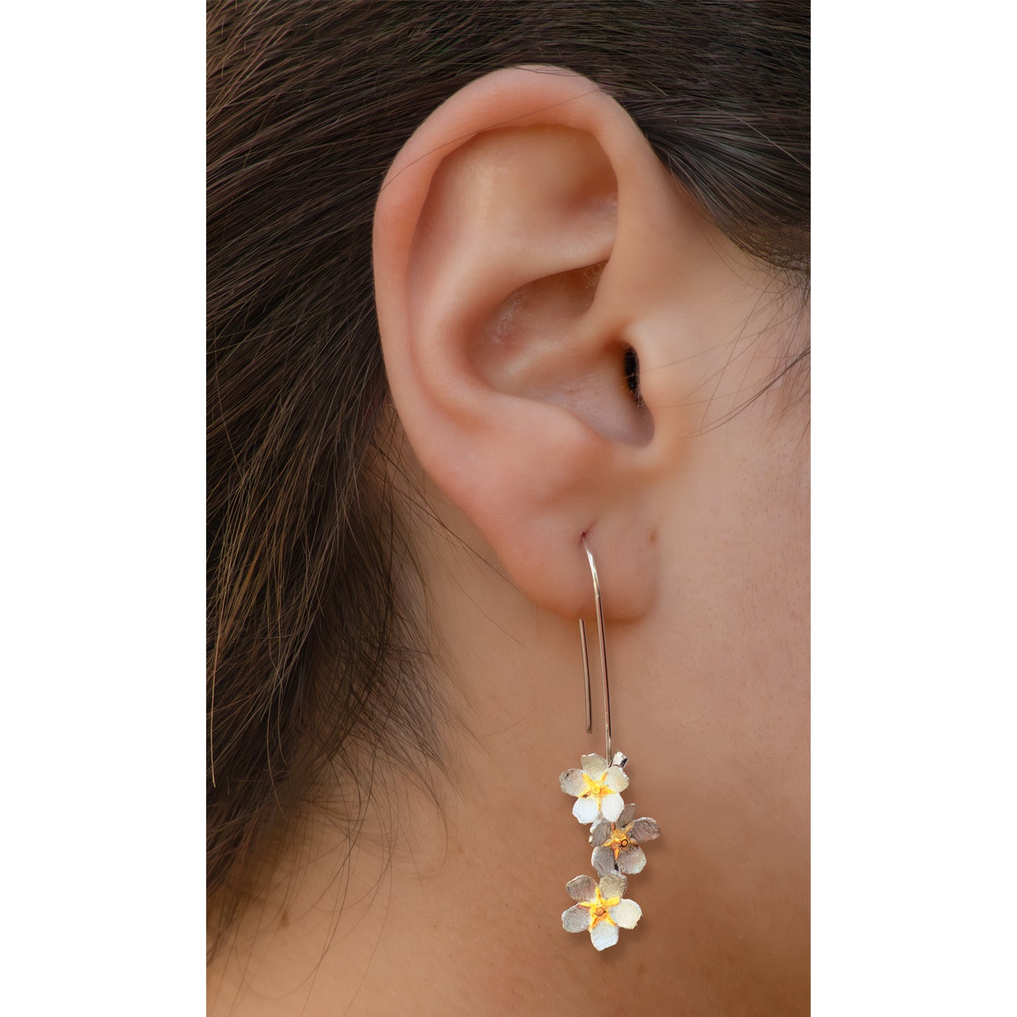Detalle de oreja con aros plateados con tres flores plateadas y centros dorados.