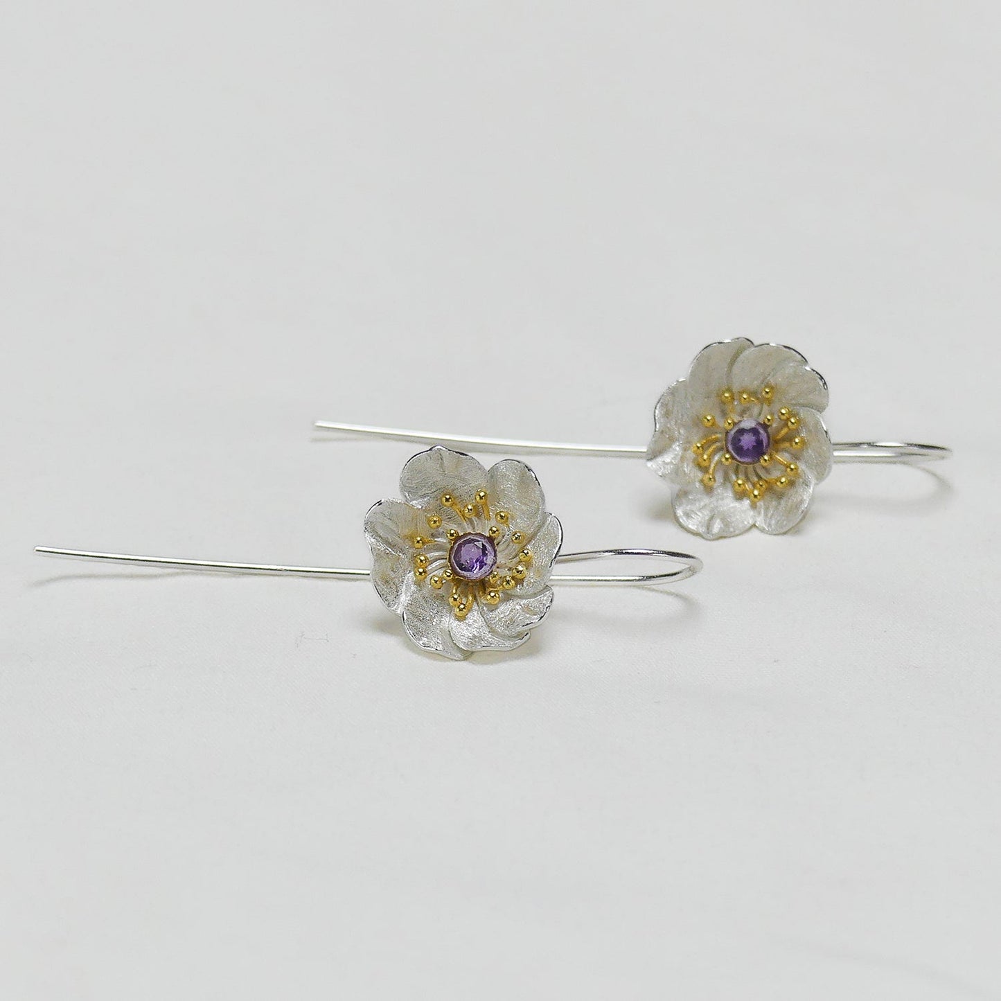 Par de aros de flores con circón morado sobre fondo gris