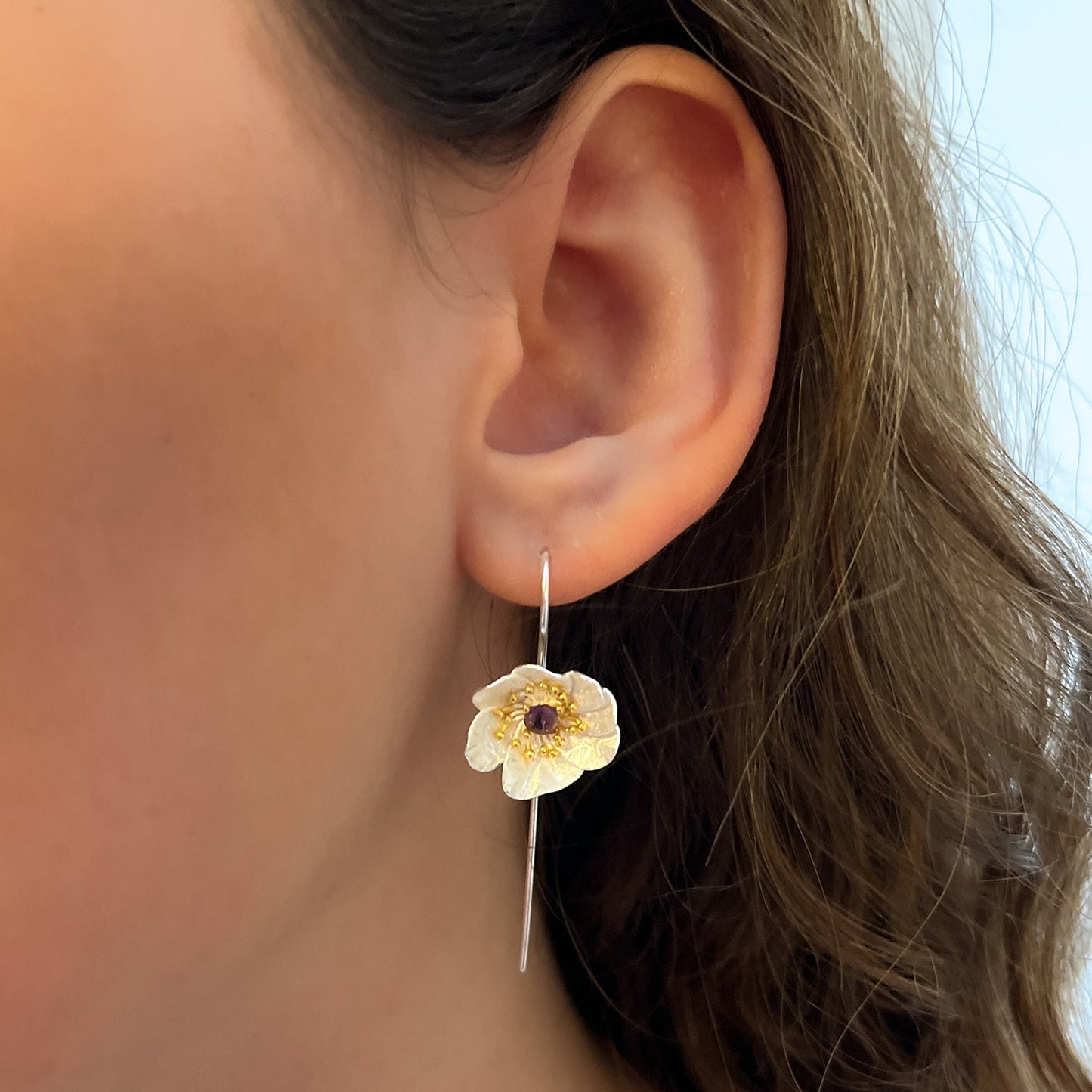 Close-up de oreja con pendiente de flor y circón morado