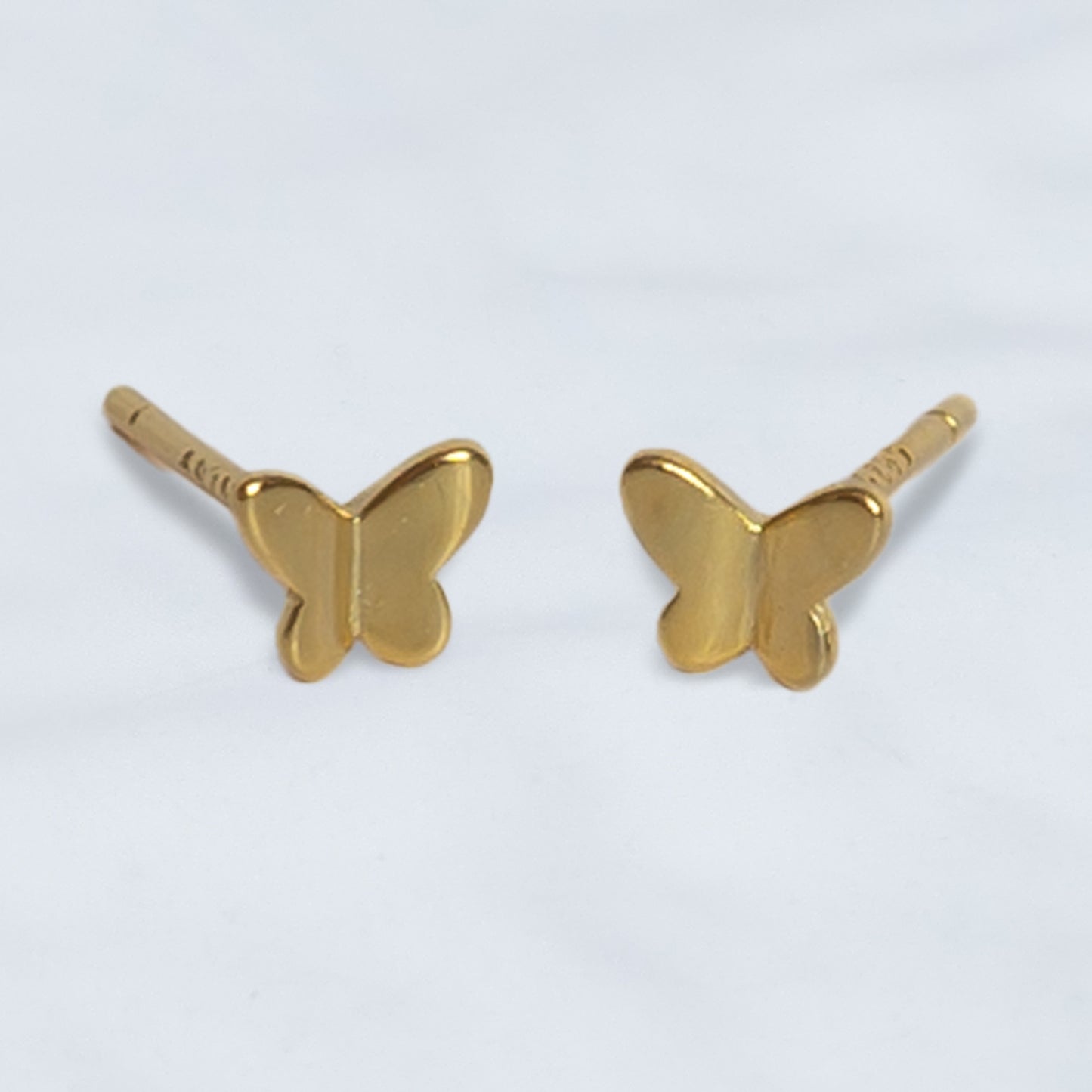 Par de pendientes de mariposa dorada con acabado brillante sobre fondo gris