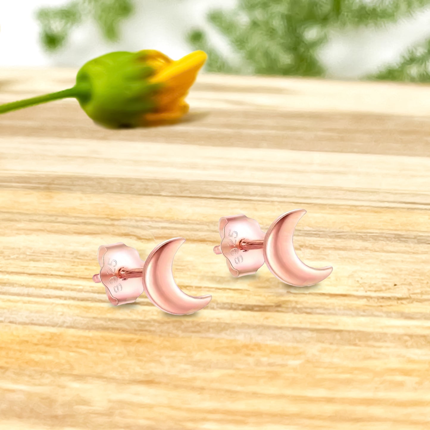 Par de aritos de media luna en oro rosado sobre madera y flor de fondo