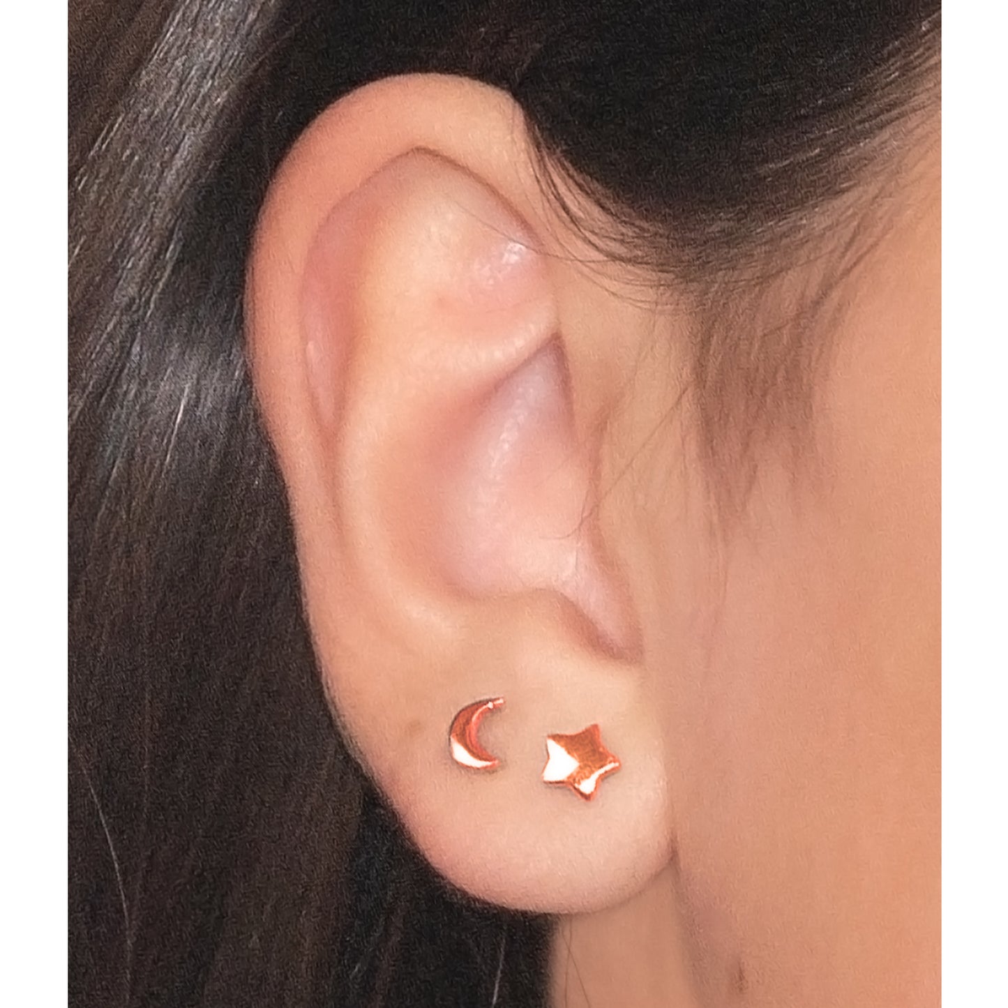 Primer plano de oreja con aritos de media luna y estrella rosada.