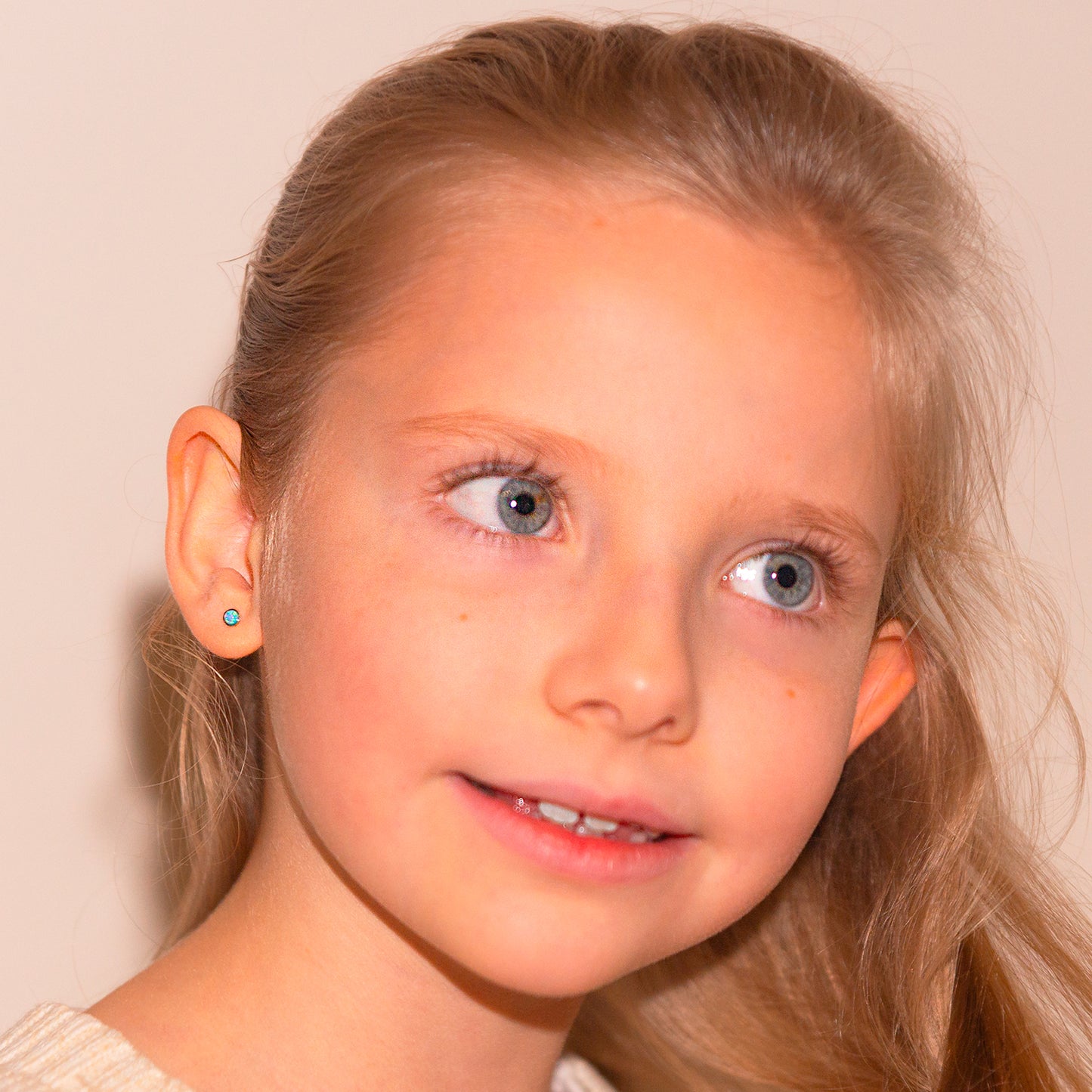 Niña rubia sonriendo usando aritos de ópalo azul