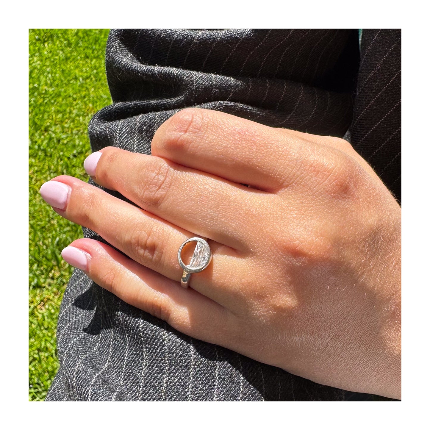 Primer plano de mano con anillo de plata y marco circular que contiene un cristal transparente.