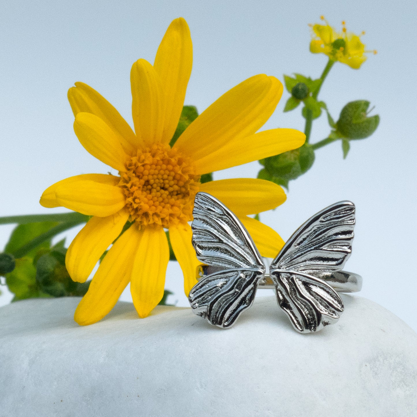 Anillo plateado con mariposa sobre piedra blanca y flor amarilla