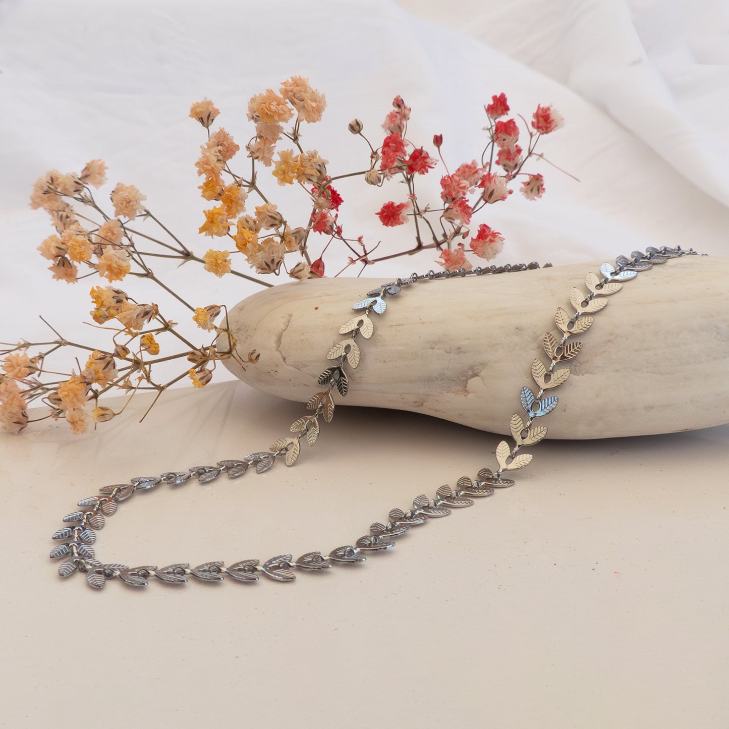 Choker plateado con hojas que forman una cadena, sobre piedra y flores secas