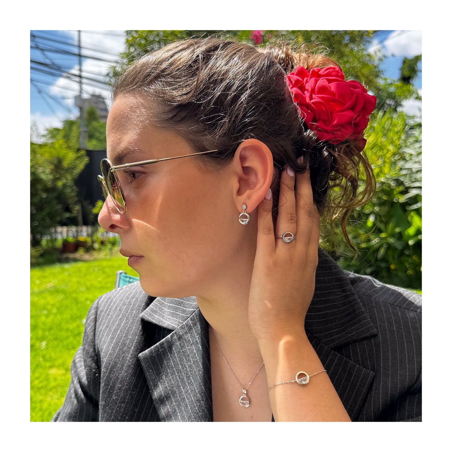 Modelo luciendo pulsera de plata con un abalorio de marco circular y un cristal transparente en su interior. Esta pulsera hace parte de un conjunto compuesto por con aros, anillo y collar.