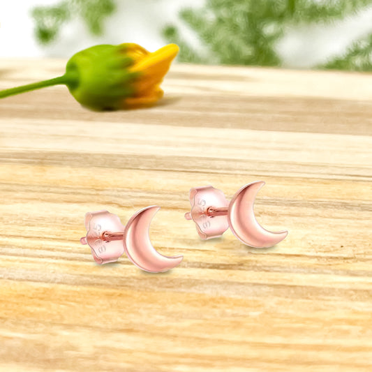Par de aritos de media luna en oro rosado sobre madera y flor de fondo